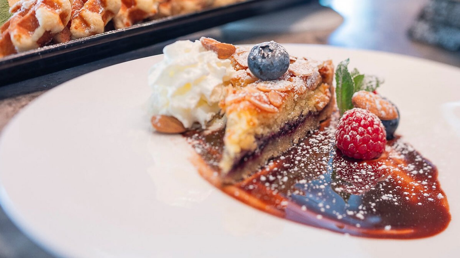 Stück Mandelkuchen mit Schlagsahne und frischen Beeren auf weißem Teller