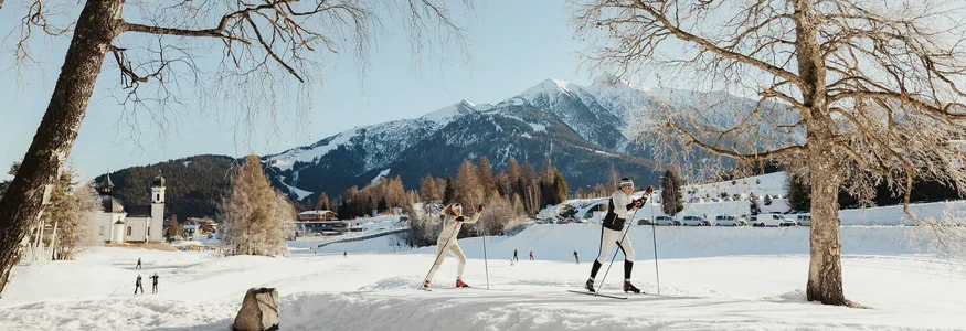 Zwei Langläufer im Schnee vor Bergen und blauen Himmel