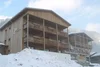 Collective enquiries © roomvisio Snow-covered wooden building with balconies against a forested mountain