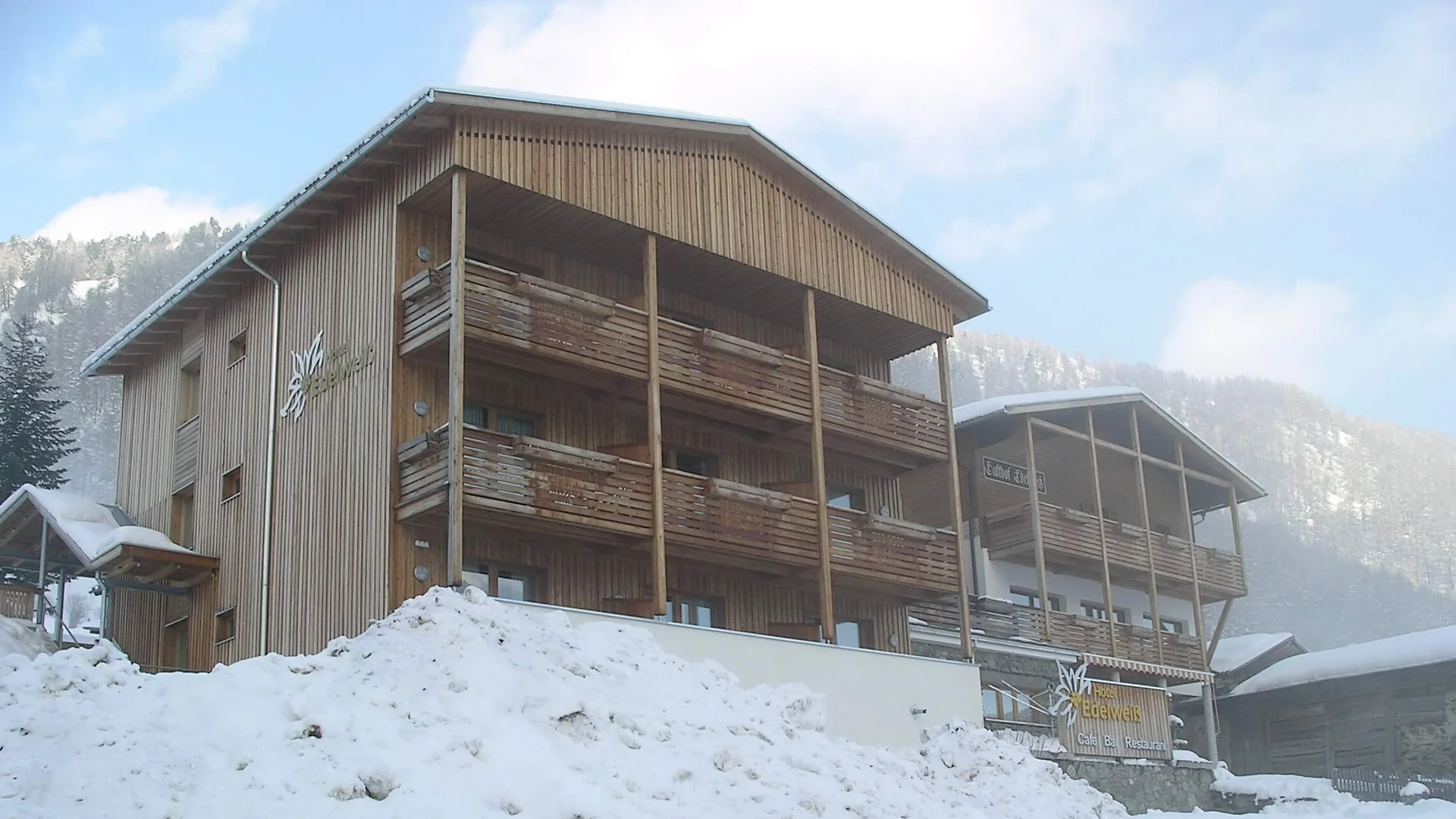 Hotel Edelweiß © roomvisio Snow-covered wooden building with balconies against a forested mountain