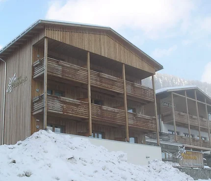 Hotel Edelweiß © roomvisio Verschneites Holzgebäude mit Balkonen vor bewaldeten Bergen
