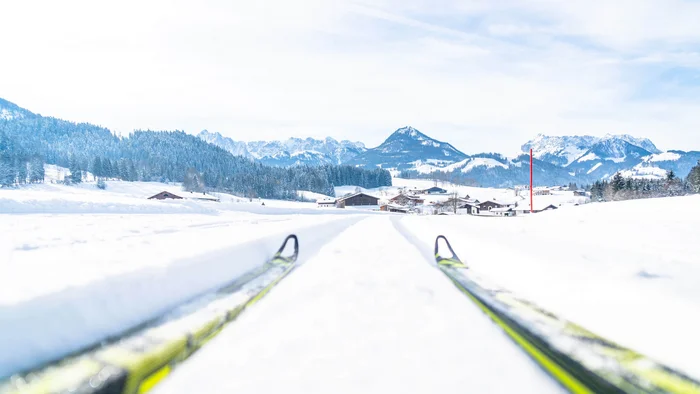 Langlaufskier auf schneebedeckter Loipe mit Bergen im Hintergrund