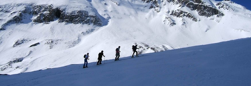 Four hikers ascending snowy slope below snow-covered mountain and clear blue sky