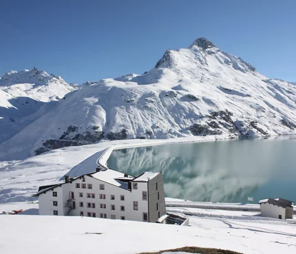 Schneebedeckte Berge und See mit weißem Gebäude im Vordergrund