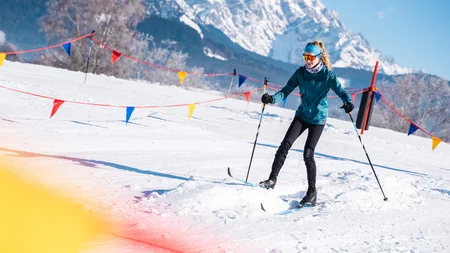 Frau beim Skilanglauf auf verschneiter Piste mit Bergen im Hintergrund