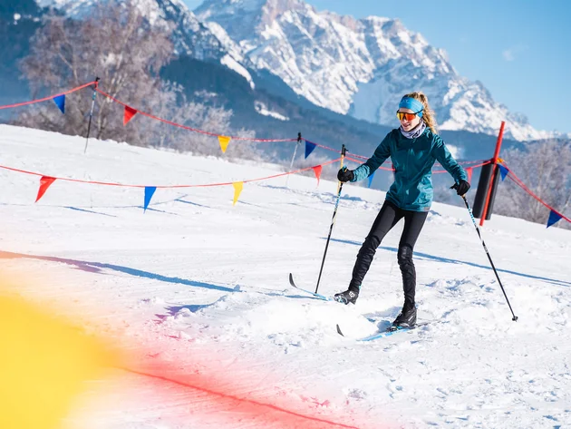 Frau beim Skilanglauf auf verschneiter Piste mit Bergen im Hintergrund