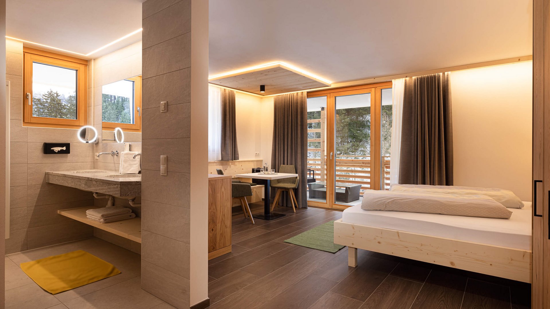 Modernes Hotelzimmer mit Doppelbett, Sitzecke, Bad und Balkon mit Waldblick