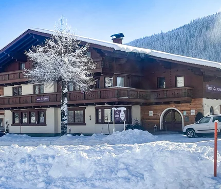 Snow-covered chalet with tree and parked cars in a winter mountain setting
