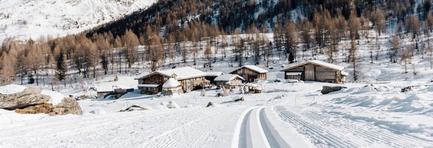 Langlaufloipe führt zu verschneiten Hütten und Bergen unter klarem Himmel