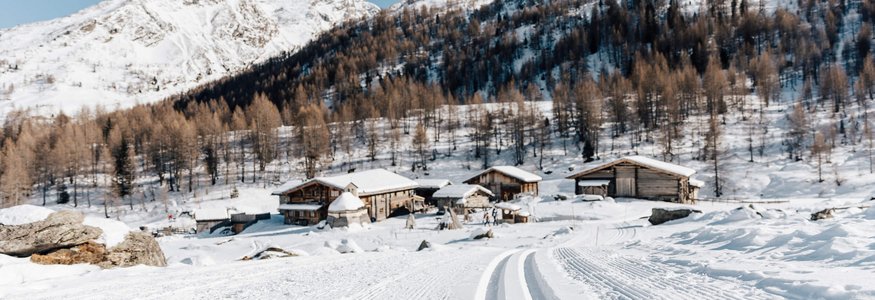 Langlaufloipe führt zu verschneiten Hütten und Bergen unter klarem Himmel