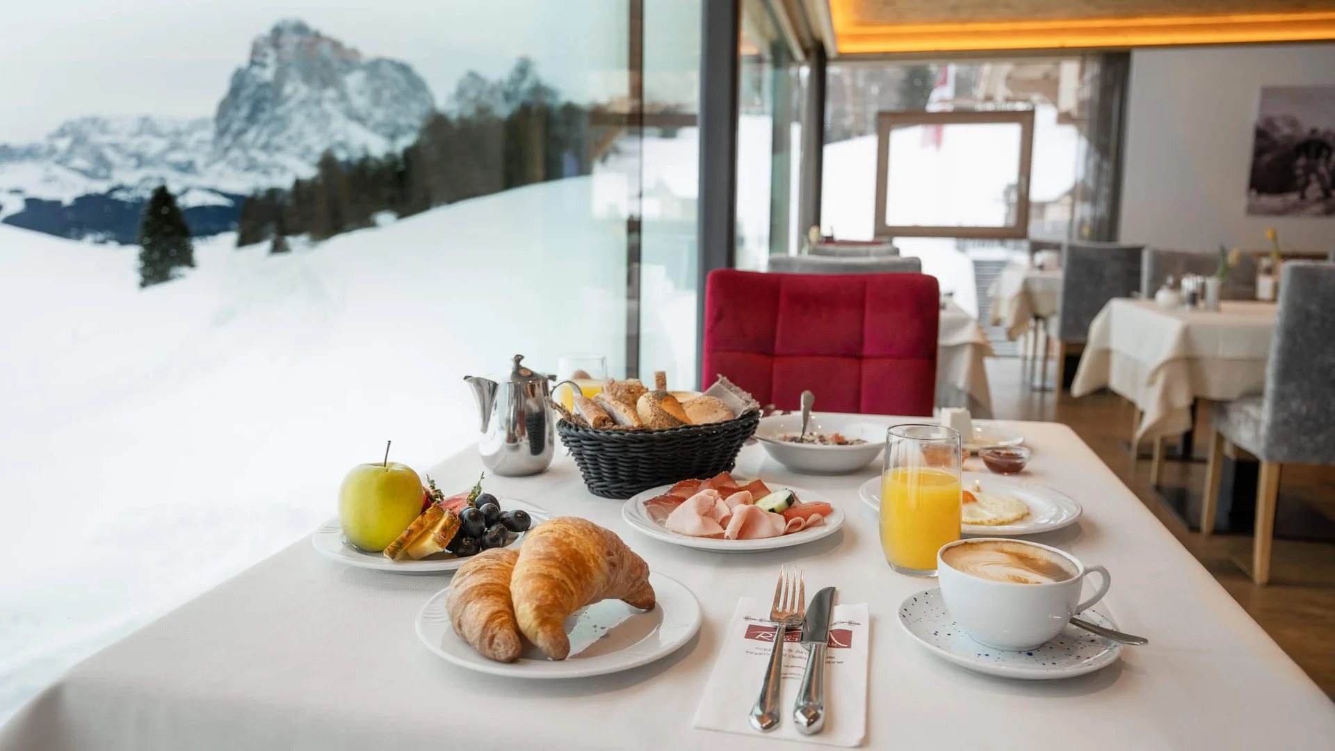 Breakfast table with croissants, fruit, cold cuts, coffee, and juice by snowy mountain view