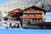 Sammelanfragen © Pension Widmann Holzhaus im Schnee vor verschneiten Bergen und klarem blauem Himmel