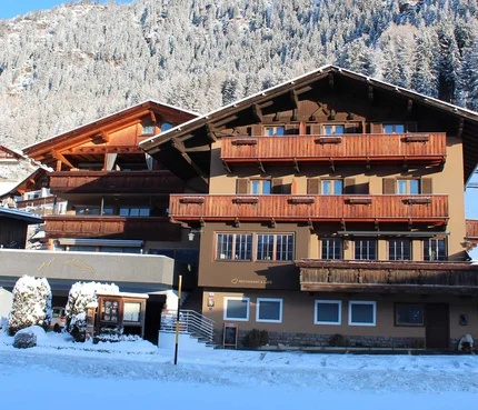 Pension Widmann © Pension Widmann Holzhaus im Schnee vor verschneiten Bergen und klarem blauem Himmel