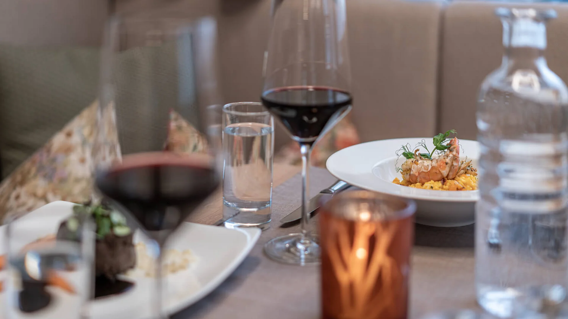 Tisch mit Glas Rotwein, Wasser, Kerze und Gourmetgericht