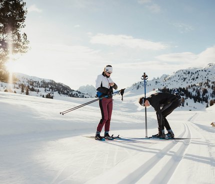 Zwei Menschen bereiten sich auf Langlauf in verschneiter Berglandschaft vor
