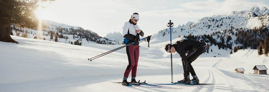 Zwei Menschen bereiten sich auf Langlauf in verschneiter Berglandschaft vor