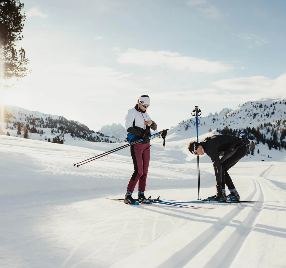 Zwei Menschen bereiten sich auf Langlauf in verschneiter Berglandschaft vor