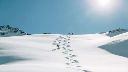 Skifahrer fährt eine Spur in frischen Pulverschnee unter klarem blauem Himmel
