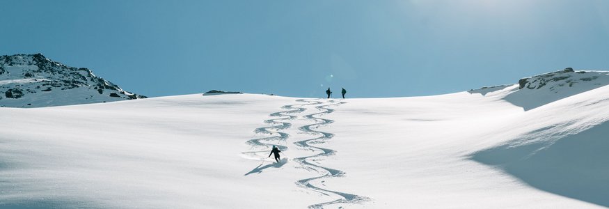 Skifahrer fährt eine Spur in frischen Pulverschnee unter klarem blauem Himmel