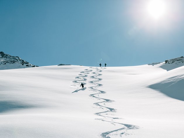 Skifahrer fährt eine Spur in frischen Pulverschnee unter klarem blauem Himmel