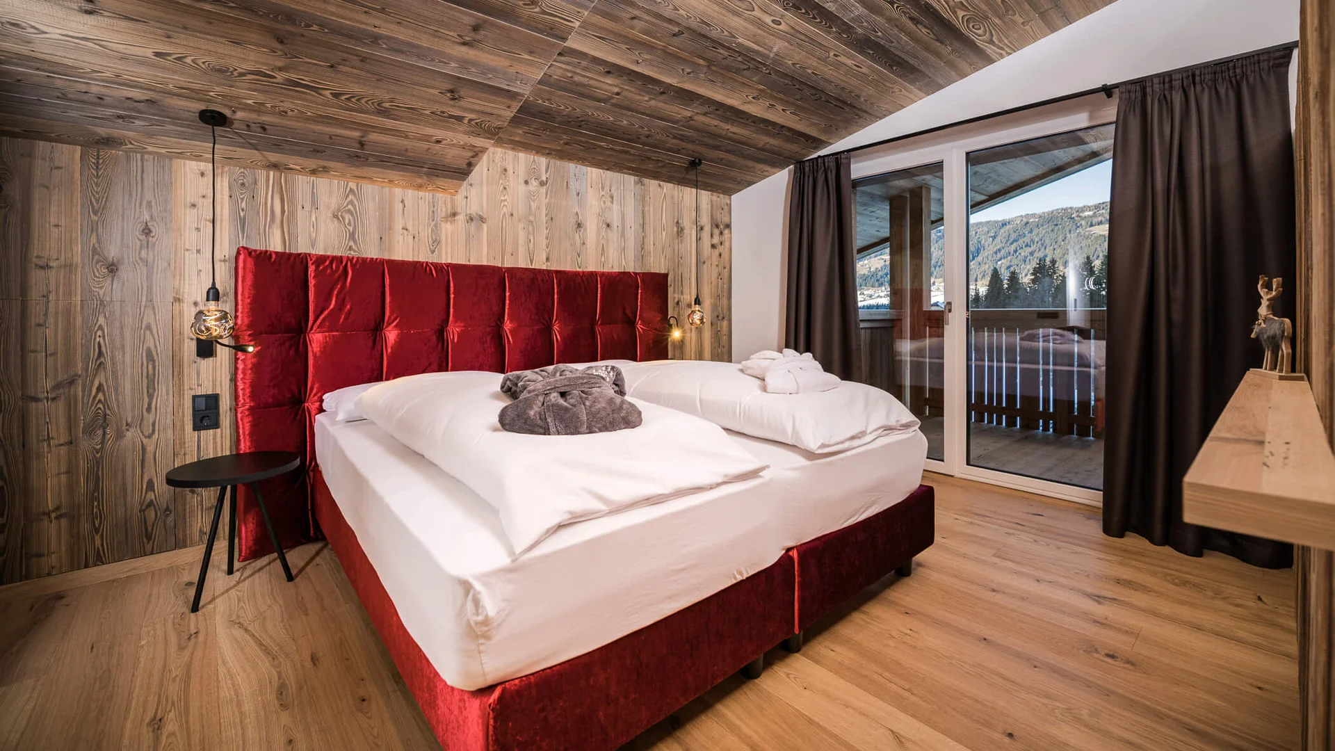 Schlafzimmer mit rotem Bett und Holzdecke, Blick auf Balkon und Berge