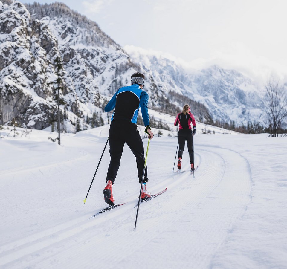 Zwei Langläufer auf verschneiter Loipe in bergiger Winterlandschaft
