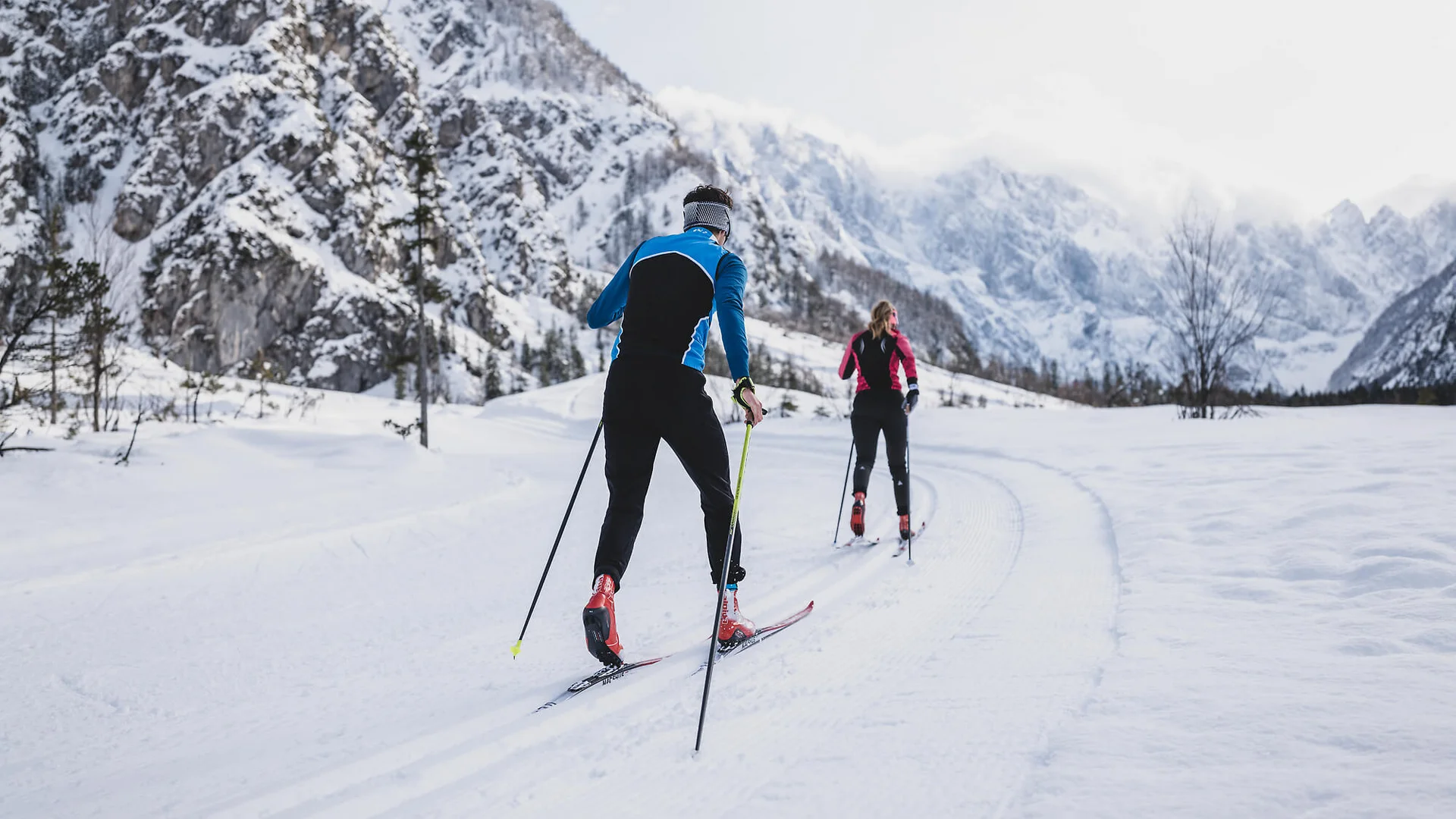 Zwei Langläufer auf verschneiter Loipe in bergiger Winterlandschaft