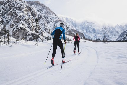 Zwei Langläufer auf verschneiter Loipe in bergiger Winterlandschaft