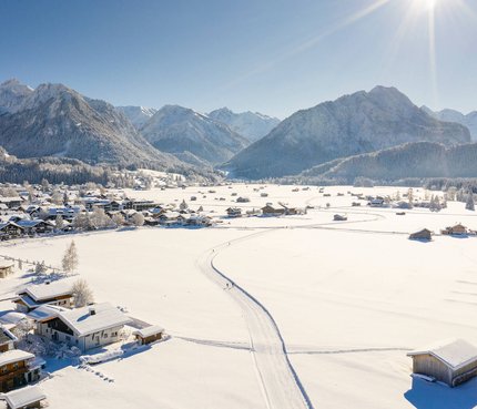 Verschneites Dorf vor Bergen bei klarem Himmel und Sonnenschein
