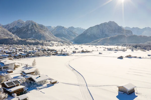 Verschneites Dorf vor Bergen bei klarem Himmel und Sonnenschein