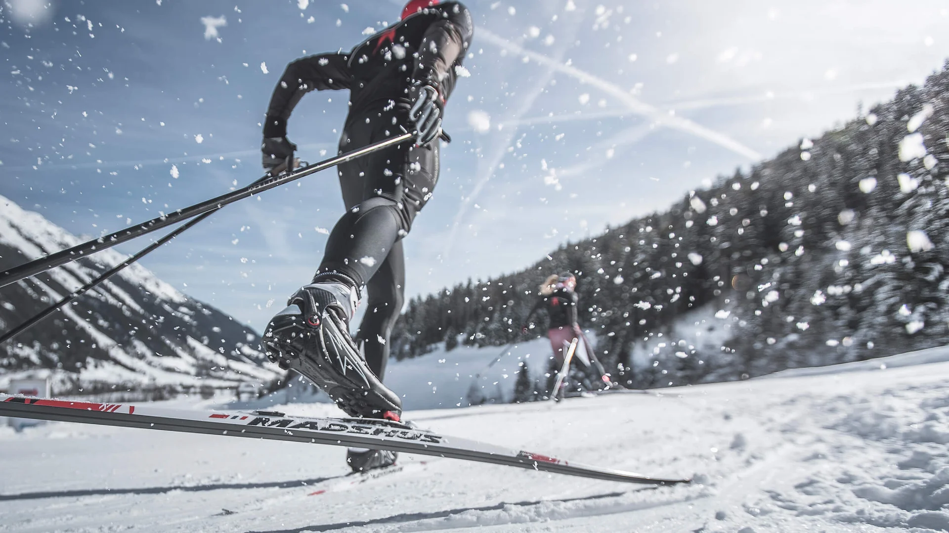 Langläufer in schwarzer Kleidung bei sonnigem Winterwetter im Schnee