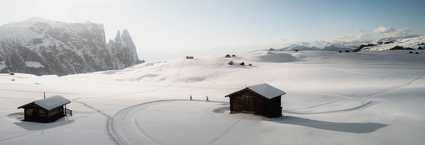 Verschneite Berghütte mit Skispuren und Berggipfeln im Hintergrund