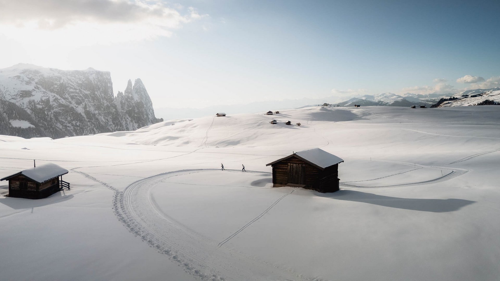 Verschneite Berghütte mit Skispuren und Berggipfeln im Hintergrund