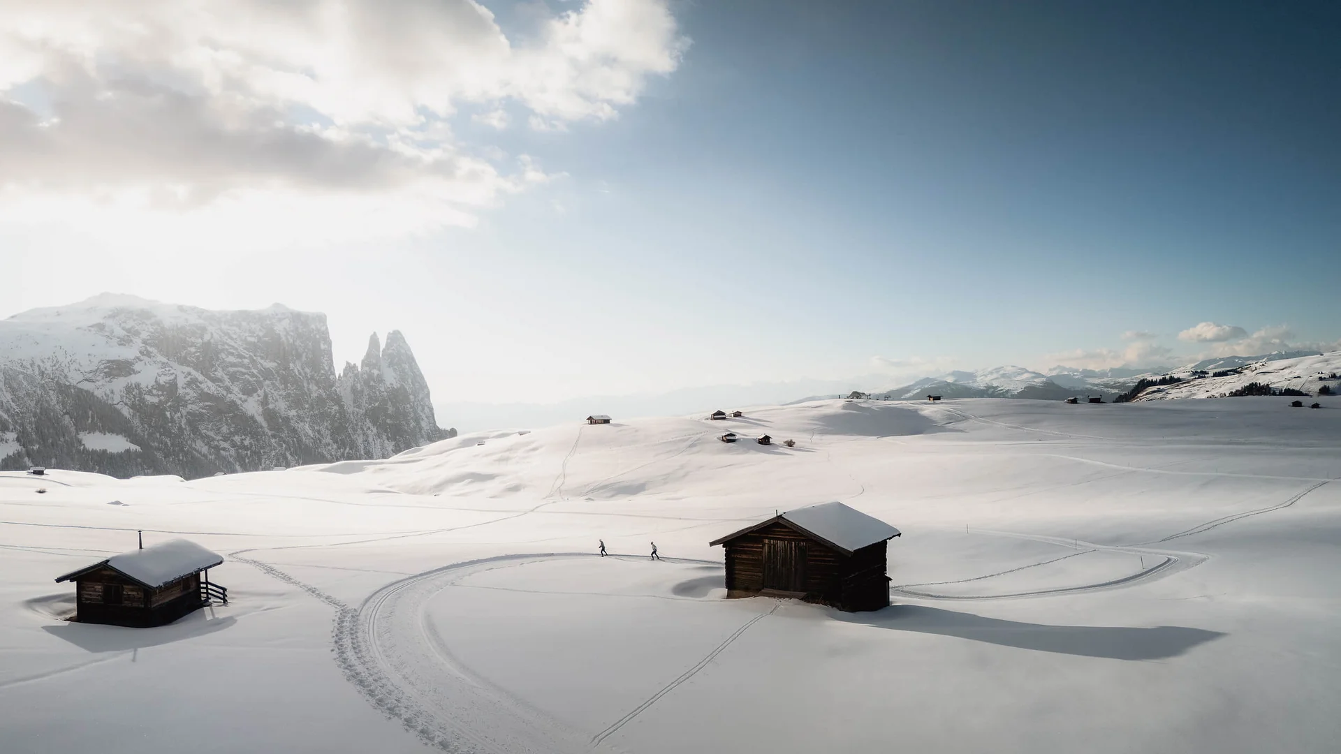 Verschneite Berghütte mit Skispuren und Berggipfeln im Hintergrund