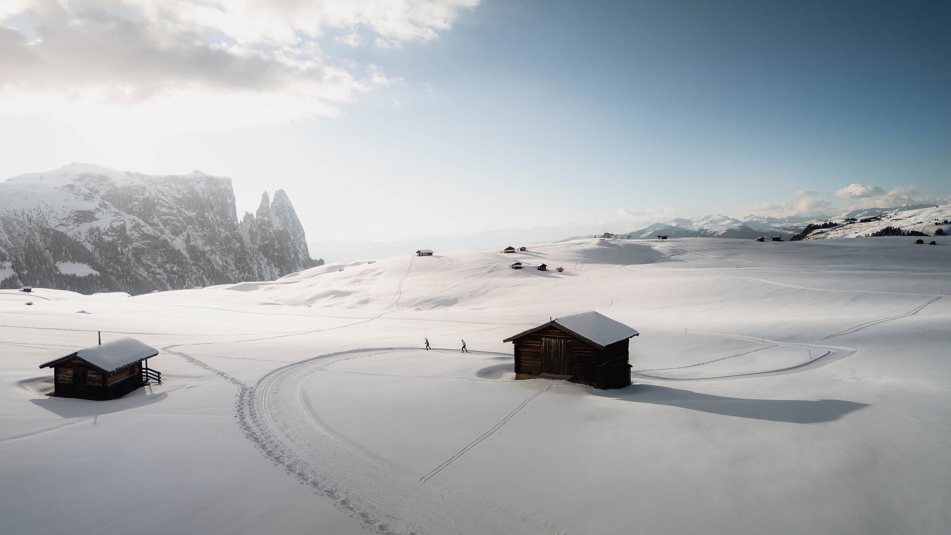 Verschneite Berghütte mit Skispuren und Berggipfeln im Hintergrund