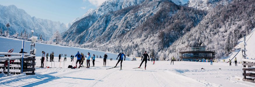 Menschen beim Langlaufen vor schneebedeckten Bergen unter klarem Himmel