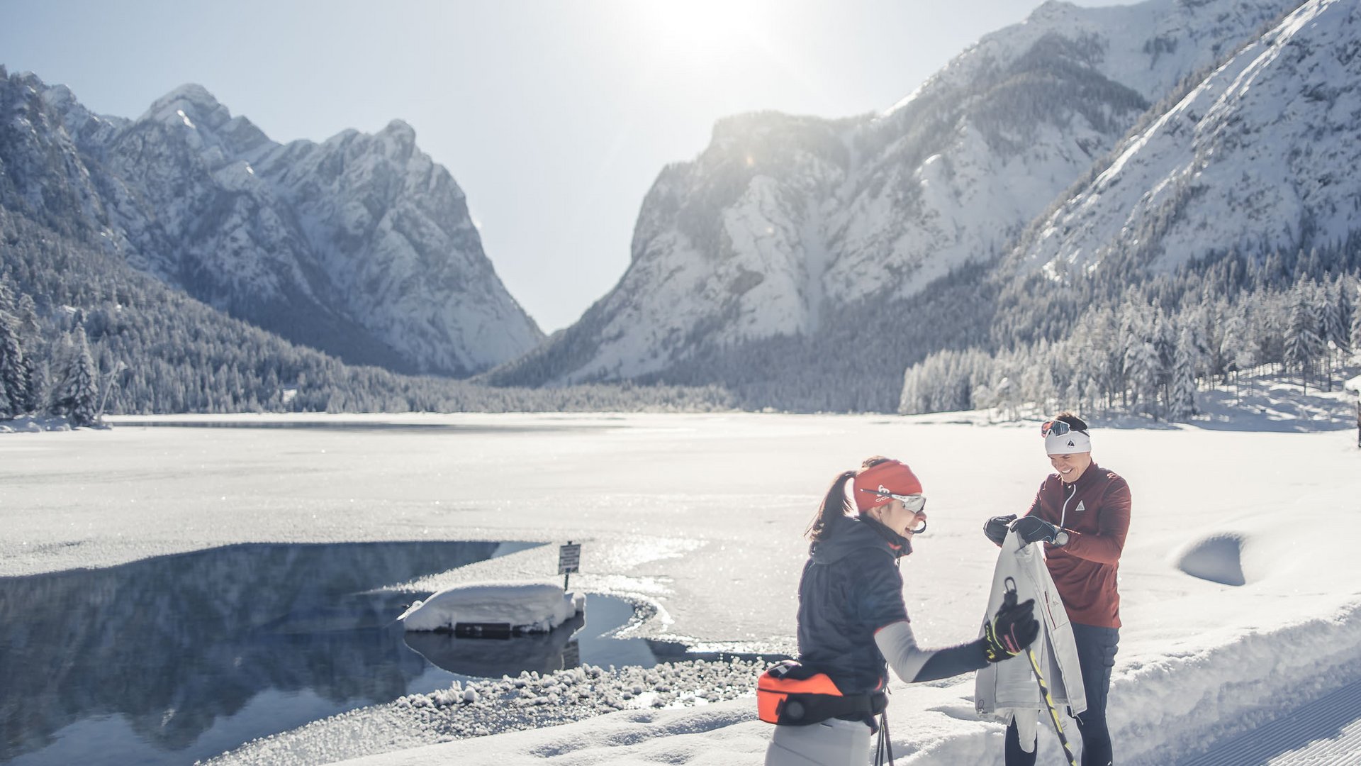 Zwei Skilangläufer in sonniger Berglandschaft mit schneebedecktem See