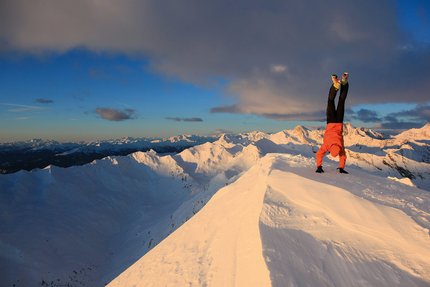 Person macht Handstand auf verschneitem Berggipfel bei Sonnenuntergang