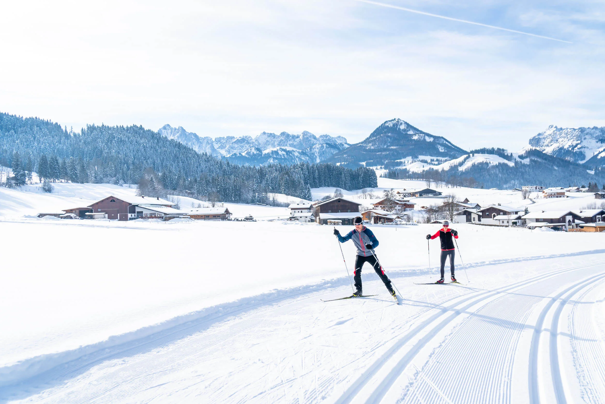Two cross-country skiers on snowy trail in alpine winter landscape