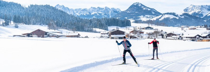 Zwei Langläufer auf verschneiter Loipe in alpiner Winterlandschaft