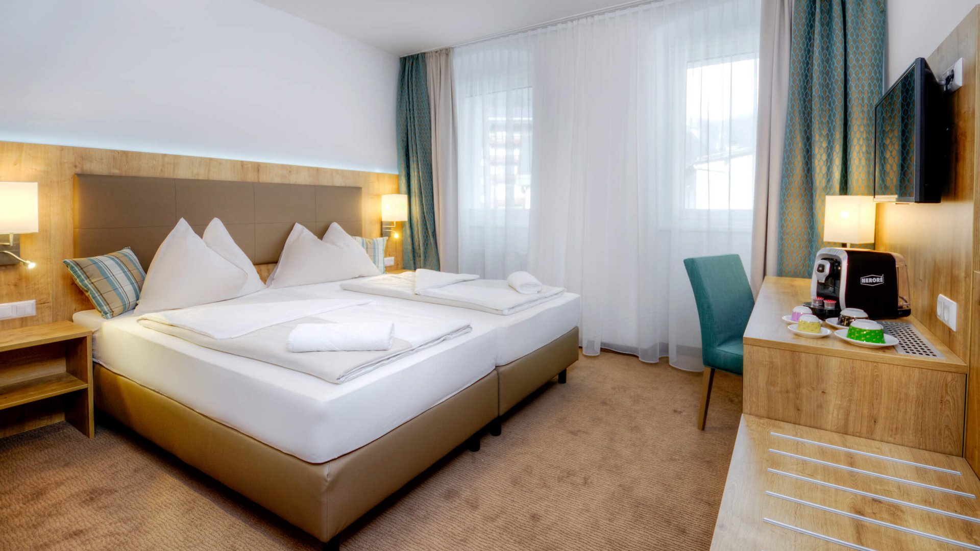 Bright hotel room with double bed, desk, coffee maker, and window with curtains