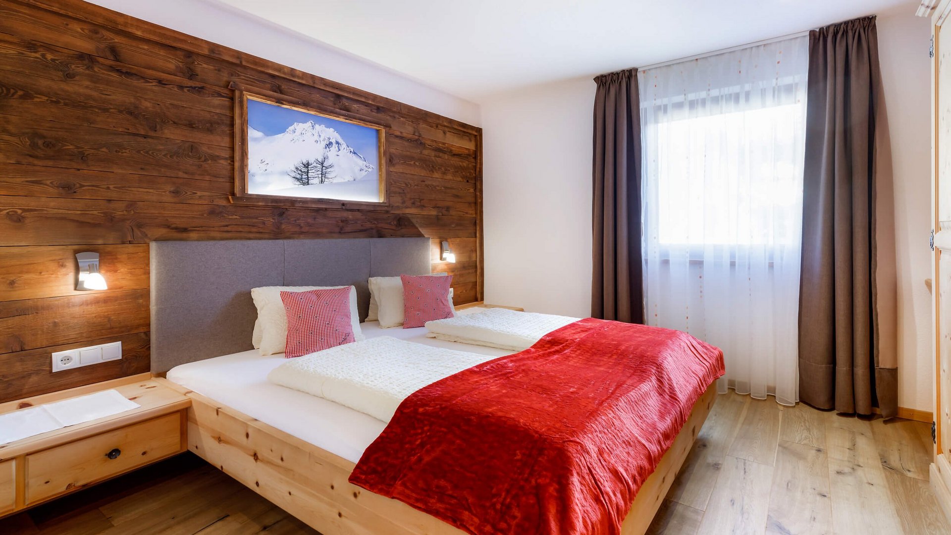 Gemütliches Schlafzimmer mit Holzwänden, Doppelbett und roter Bettdecke