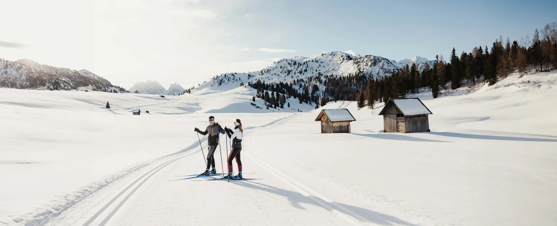Zwei Skifahrer auf gespurter Loipe in verschneiter Berglandschaft mit Hütten