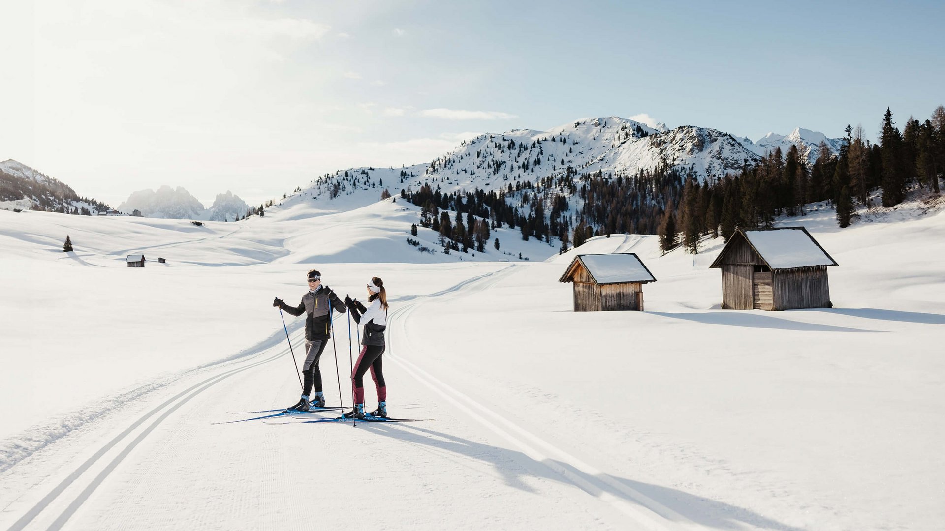 Zwei Skifahrer auf gespurter Loipe in verschneiter Berglandschaft mit Hütten