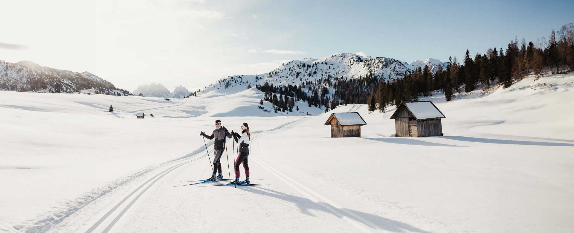 Zwei Skifahrer auf gespurter Loipe in verschneiter Berglandschaft mit Hütten