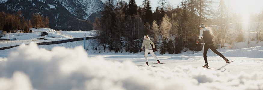 Two people cross-country skiing in snowy mountains with sunlight