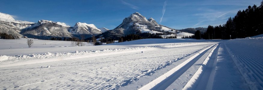 Gespurte Ski- und Schneelaufloipe mit schneebedeckten Bergen im Hintergrund