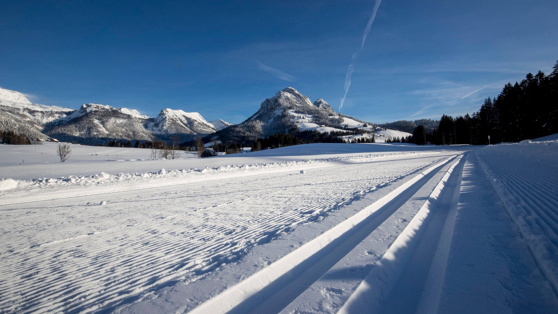 Gespurte Ski- und Schneelaufloipe mit schneebedeckten Bergen im Hintergrund