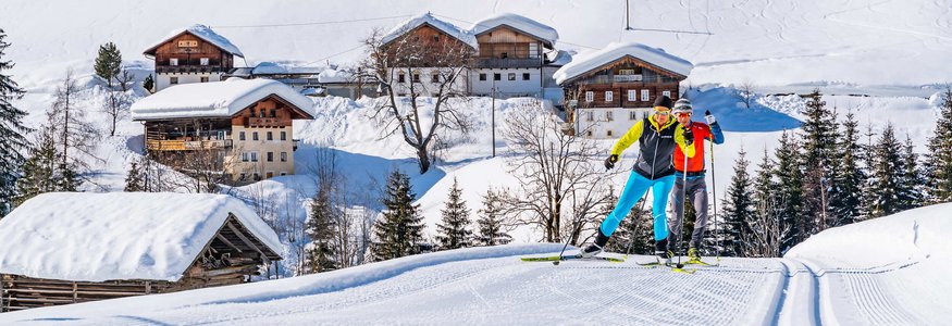 Zwei Langläufer auf einer Spur vor verschneiten Häusern und Bergen
