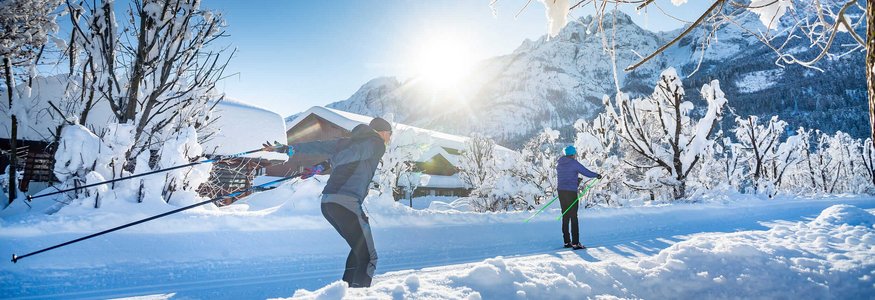 Two people cross-country skiing in a snowy mountain landscape with sunshine